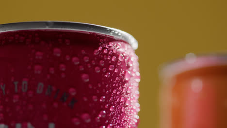 Close-Up-Of-Condensation-Droplets-On-Revolving-Takeaway-Cans-Of-Cold-Beer-Or-Soft-Drinks-Against-Yellow-Background